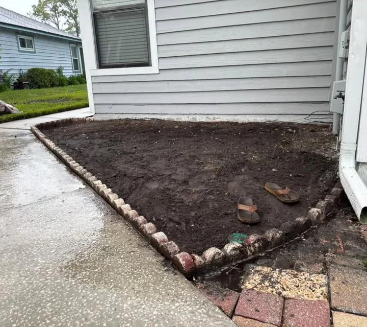 A prepared garden bed with stone edging beside a home